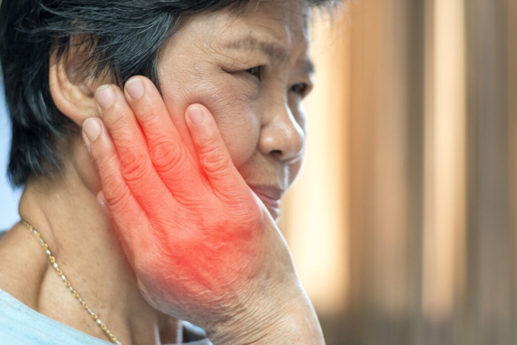 TMJ & Jaw Disorders Asian woman with pain in cheek and irritation on hand